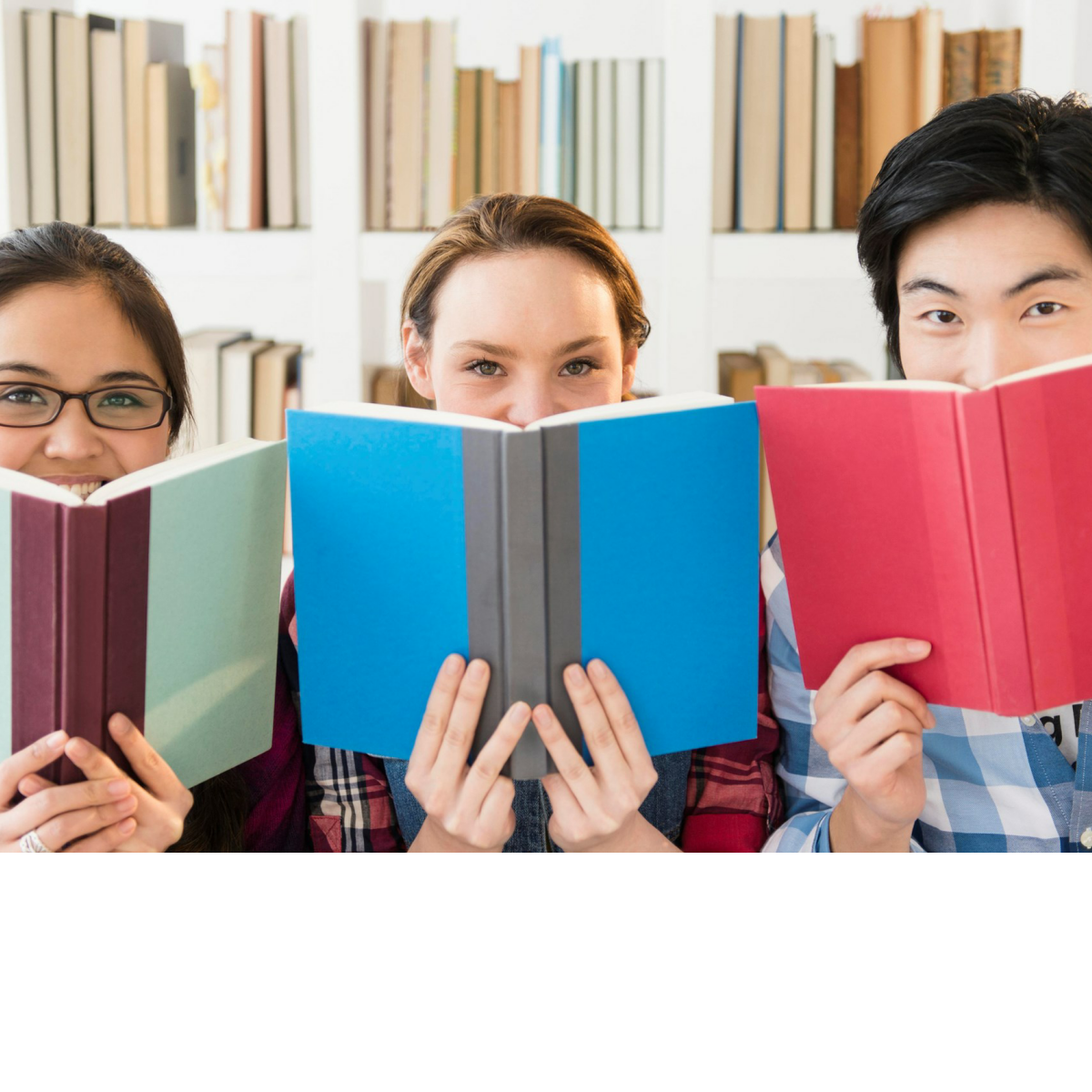 Photo of 3 smiling teens with books in front of their faces